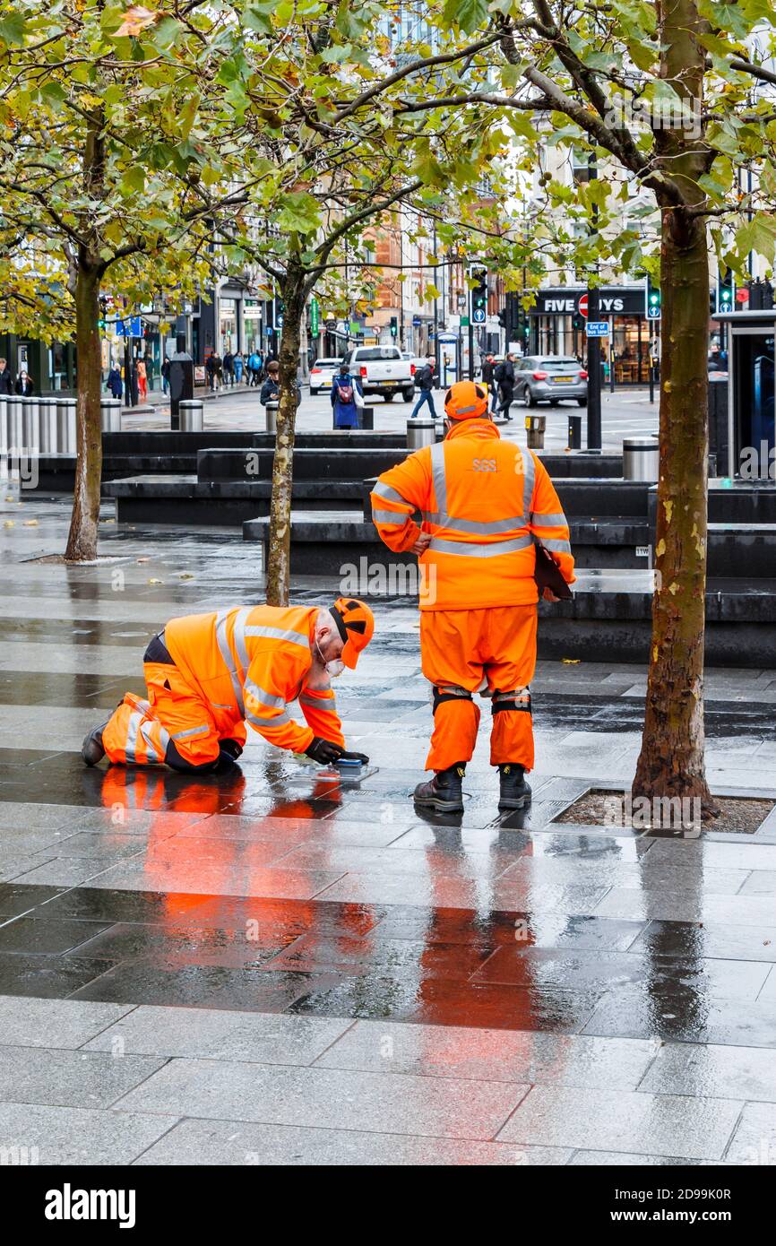 Two male employees of SGS in orange high-visibility clothing, making an inspection on the forecourt of King's Cross Station, London, UK Stock Photo