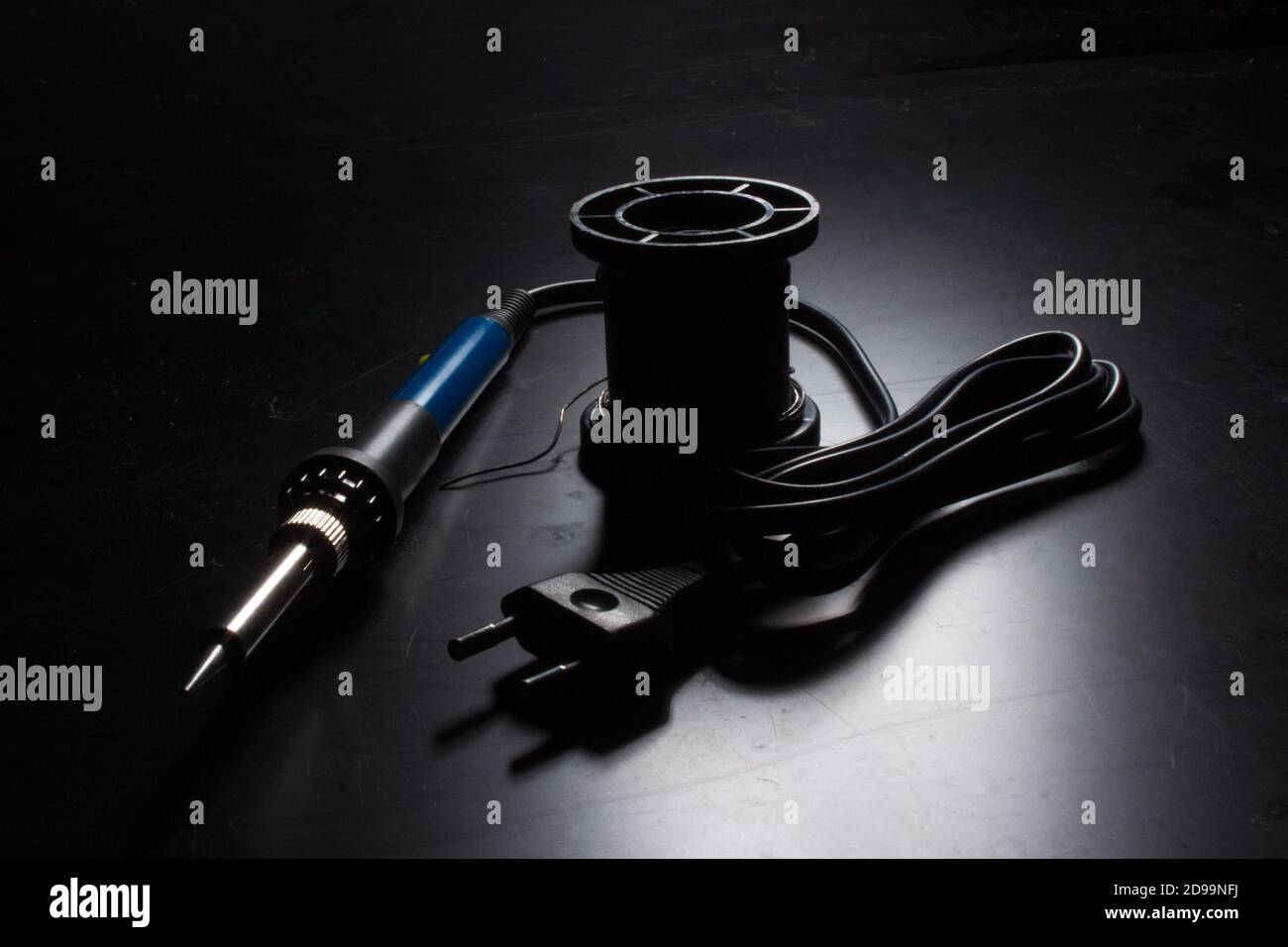 A soldering iron with a blue handle and a coil of solder on the old black desktop surface. Back