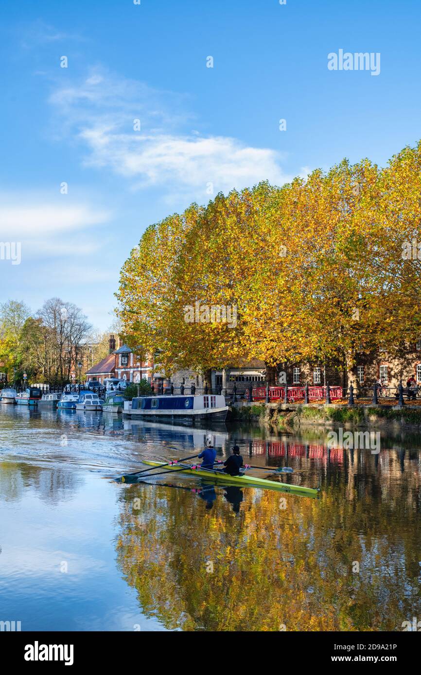 Narrowboat and rowers on the river thames at St Helens Wharf at sunrise in the autumn. Abingdon on Thames, Oxfordshire, England Stock Photo