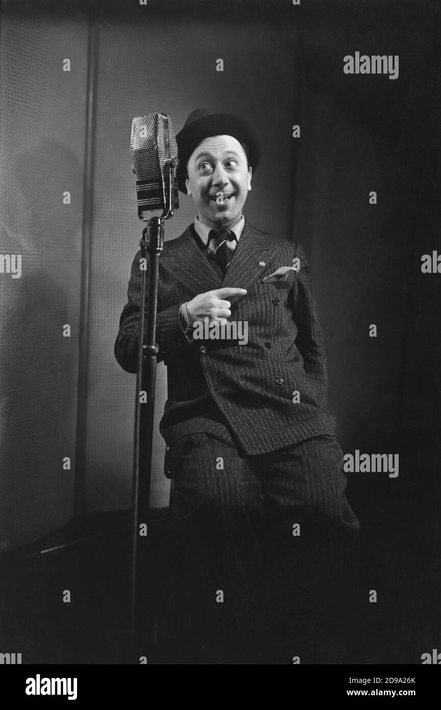 1940 ca , ITALY : The italian comician theatre and movie actor ERMINIO MACARIO ( Torino , 1902 - 1980 ) at EIAR radio . In this photo have the pinn badge of PARTITO NAZIONALE FASCISTA ( PNF ), the fascist Party symbol . - CINEMA - TEATRO - THEATRE - THEATER - MOVIE - CINEMA - COMICO - attore comico - hat - cappello - hat - cappello - cravatta - tie - microphone - microfono - trasmissione radiofonica - smile - sorriso - FASCISMO - FASCISTA - FASCISM - FASCIST - PROPAGANDA RADIOFONICA  © Archivio GBB / Stock Photo