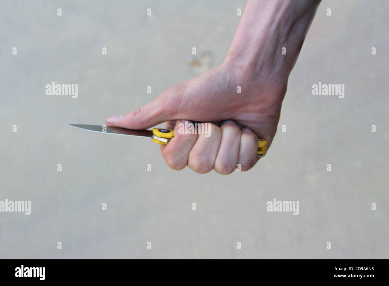 The man's hand holds a knife. Fingers compress a folding knife with a shiny close-up blade. The concept of crime, assault, weapons, security and attempted murder. Stock Photo