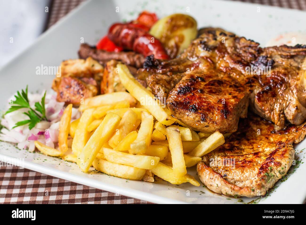 Traditional Balkan mixed grill dish - different types of bbq meat and vegetables with fries, selective focus Stock Photo
