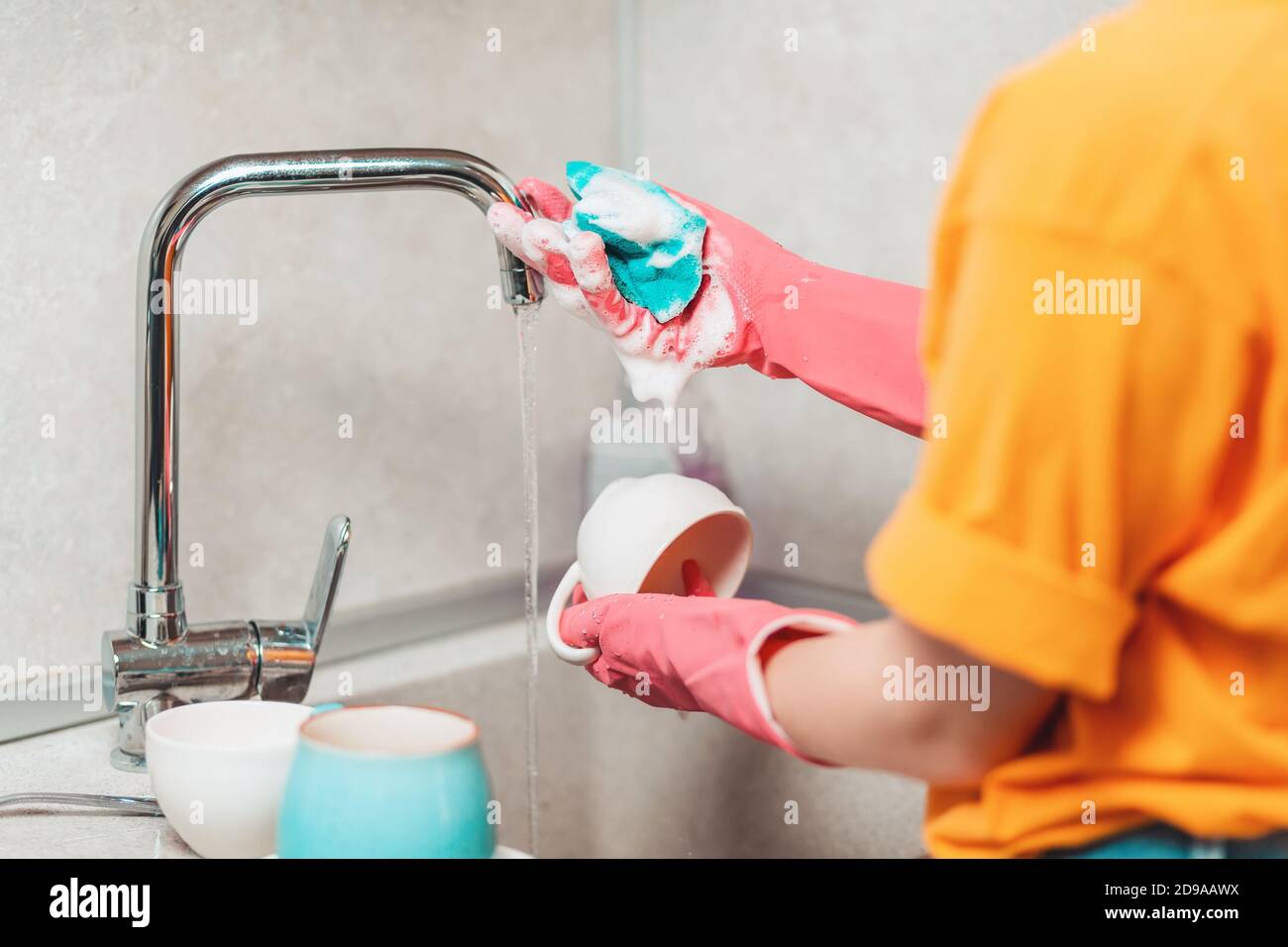 A woman in pink rubber gloves is washing dishes. Close up. View from