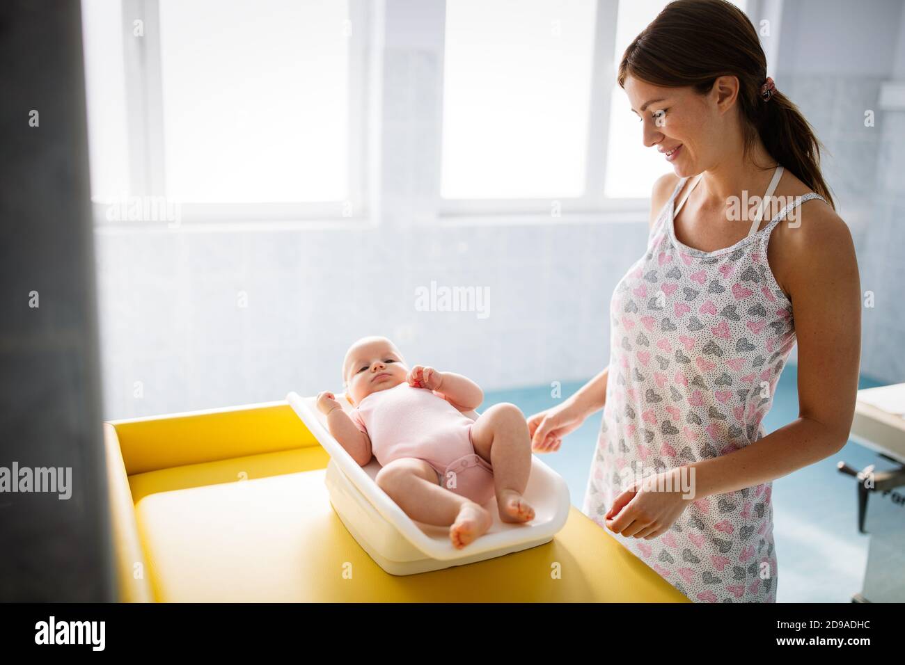 Mother weighting cute baby on scales in room Stock Photo