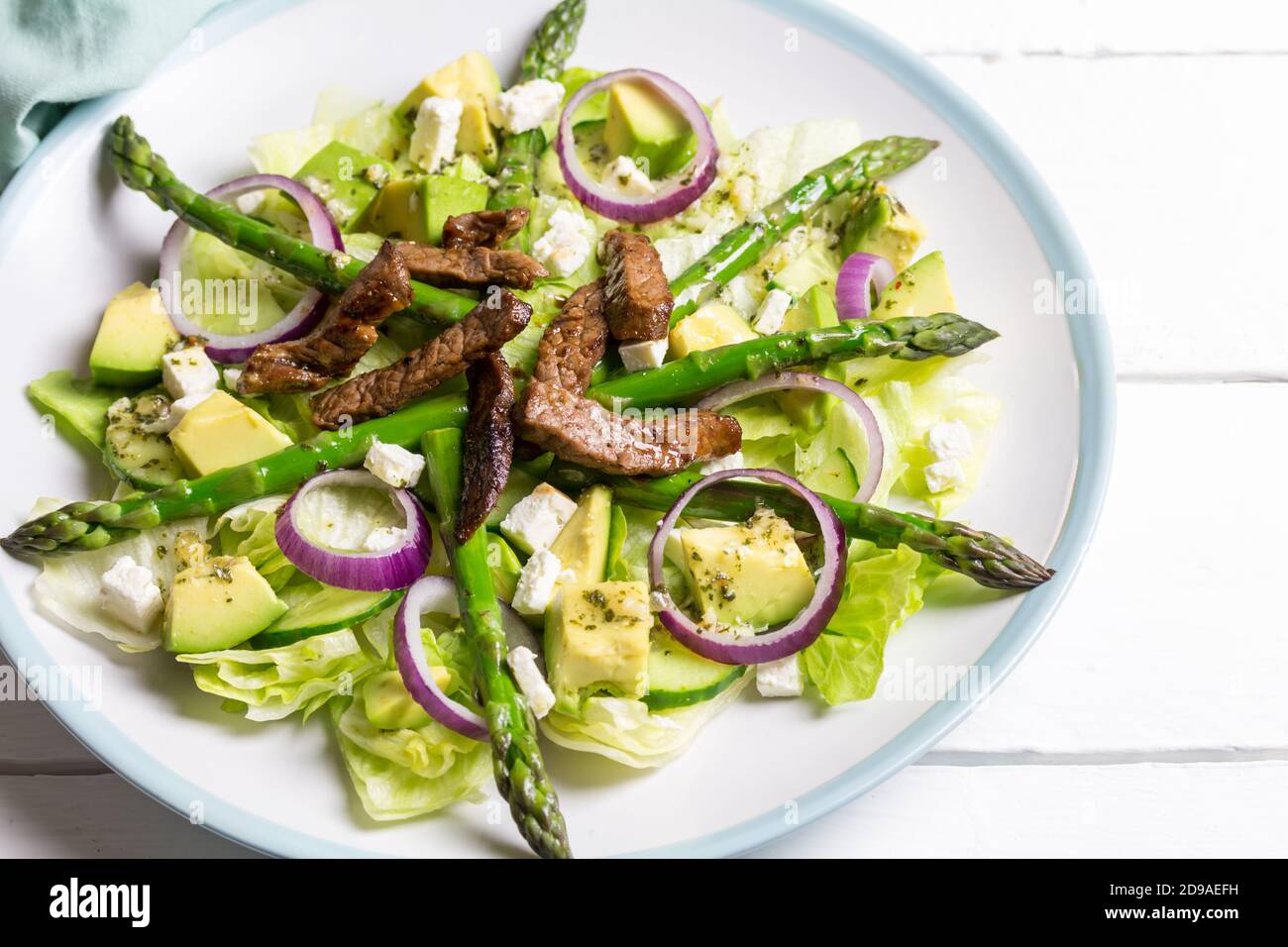 Asparagus salad with avocado, steak strips, red onion and lettuce on white table with space for text Stock Photo