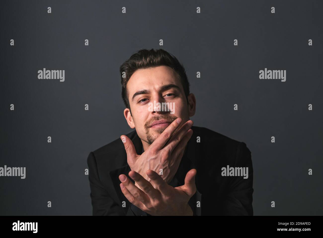 Studio portrait of a young caucasian man in a black jacket, looking at the camera, against plain studio background Stock Photo