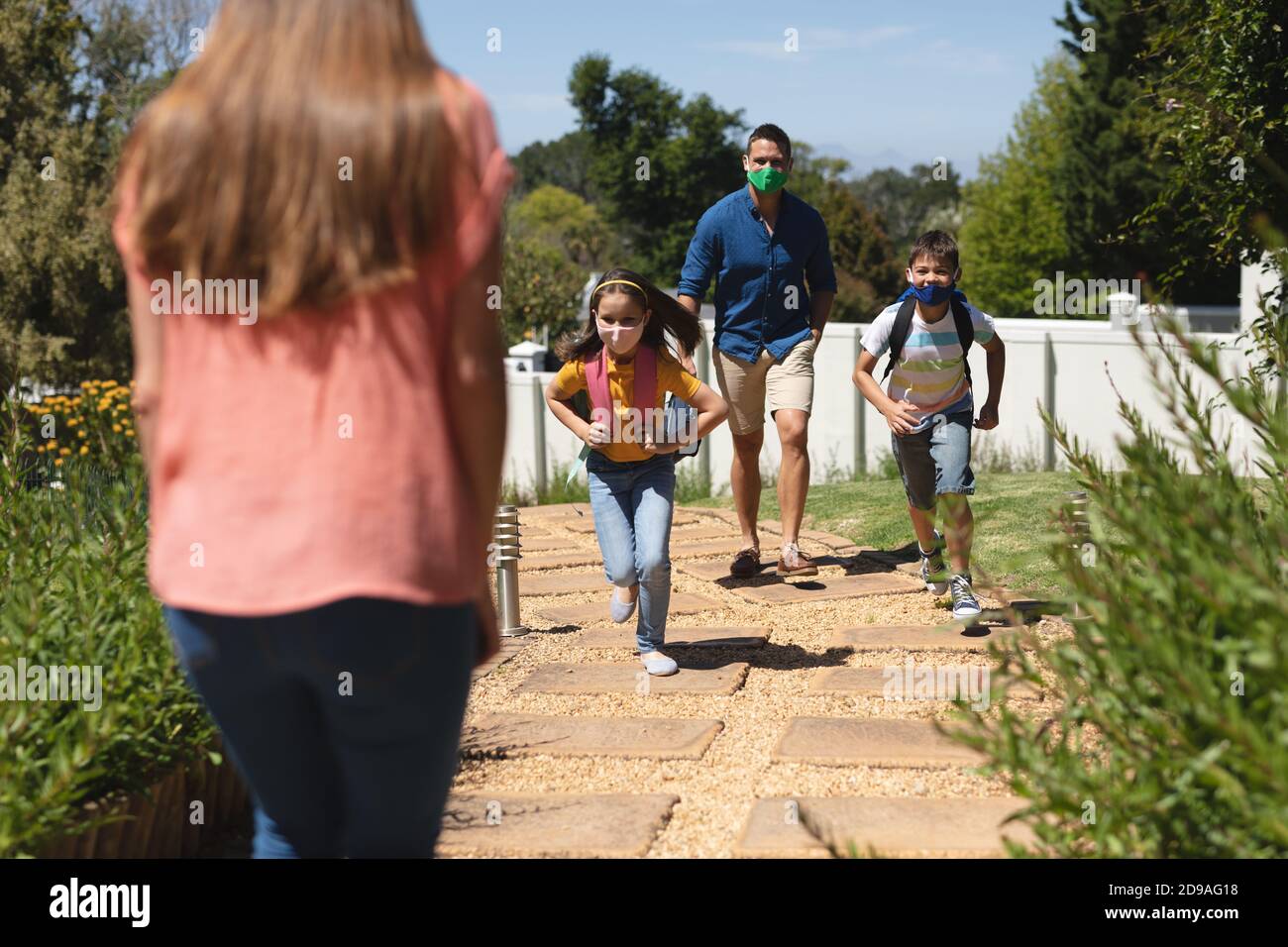 Caucasian boy and girl running to mother after retunring home from school with their father Stock Photo