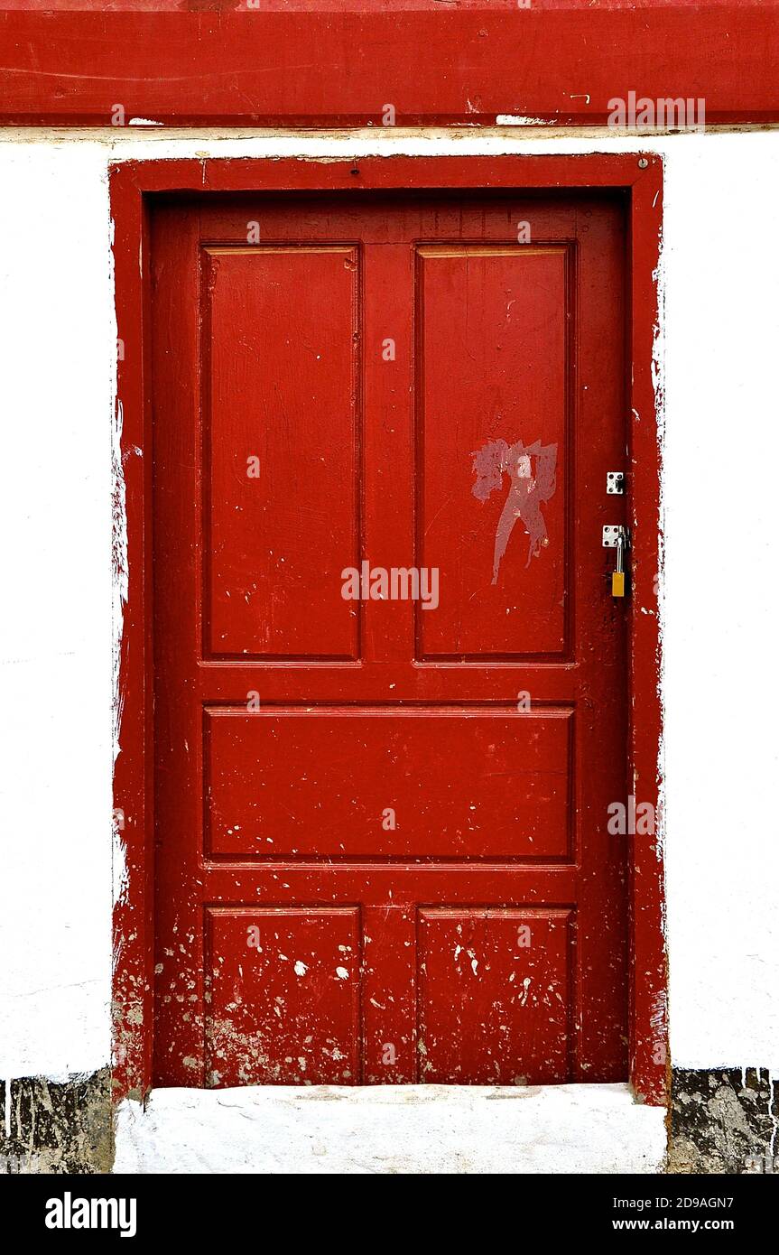 A locked paint splattered red wooden door in a rustic white stone building. Stock Photo
