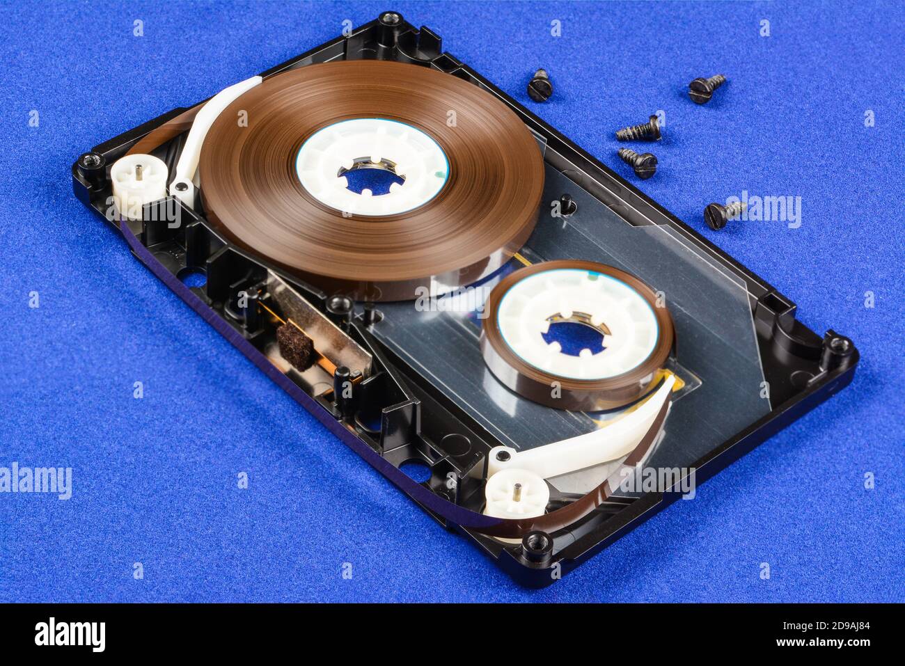 Disassembled audio compact cassette with SM mechanism. Audio cassette with tape guide as security mechanism and screws. on blue background. Stock Photo