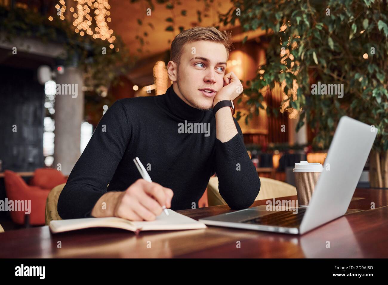 Successful young guy sits in cafe by table with his laptop on it Stock Photo