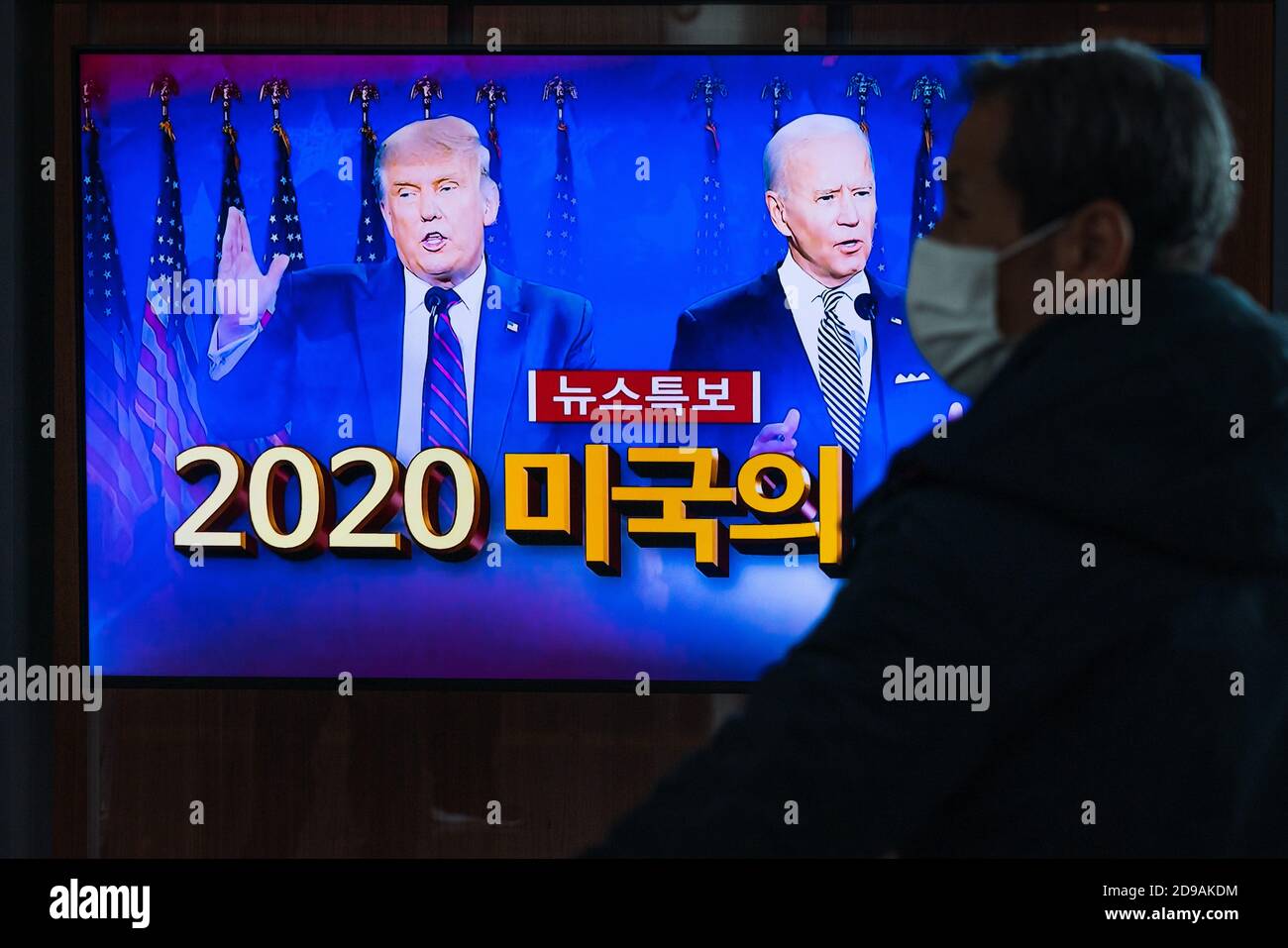 A man wearing a mask at Seoul Train Station watches news report about the US presidential election comparing Joe Biden with Donald Trump on 2020 US presidential election day. Stock Photo