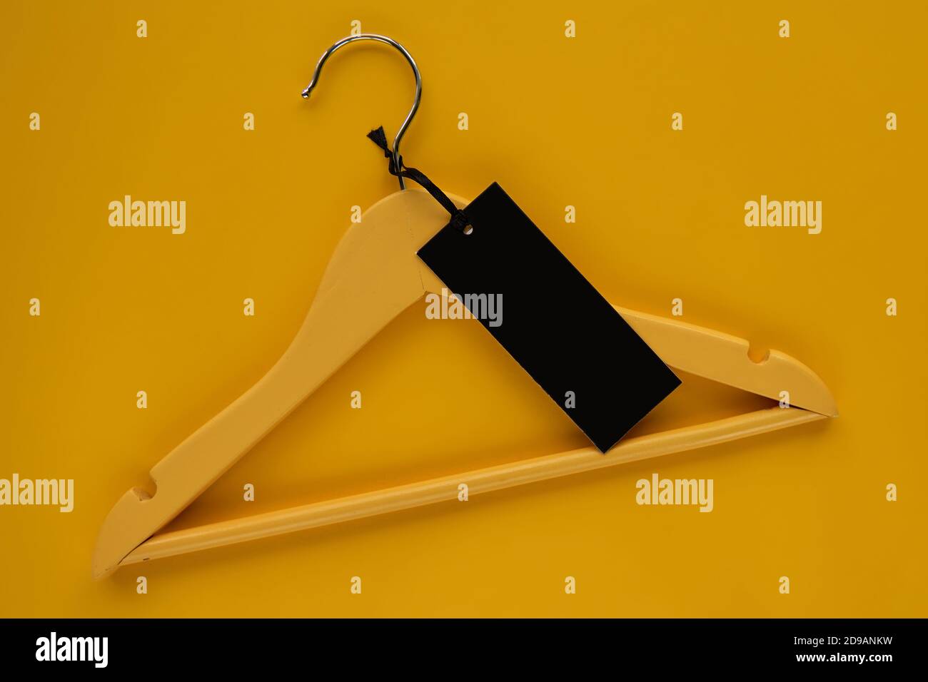 Wooden Coat hanger with black paper label isolated on yellow paper background. Clothing tag, label blank mockup template, to place your design. Black Stock Photo