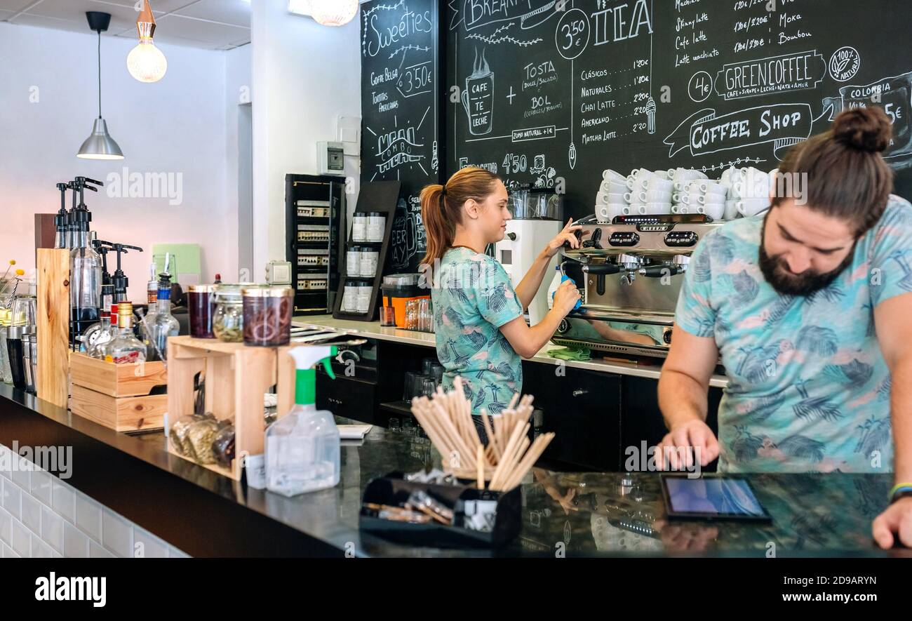 Waitress preparing coffee machine while her coworker uses the tablet Stock Photo