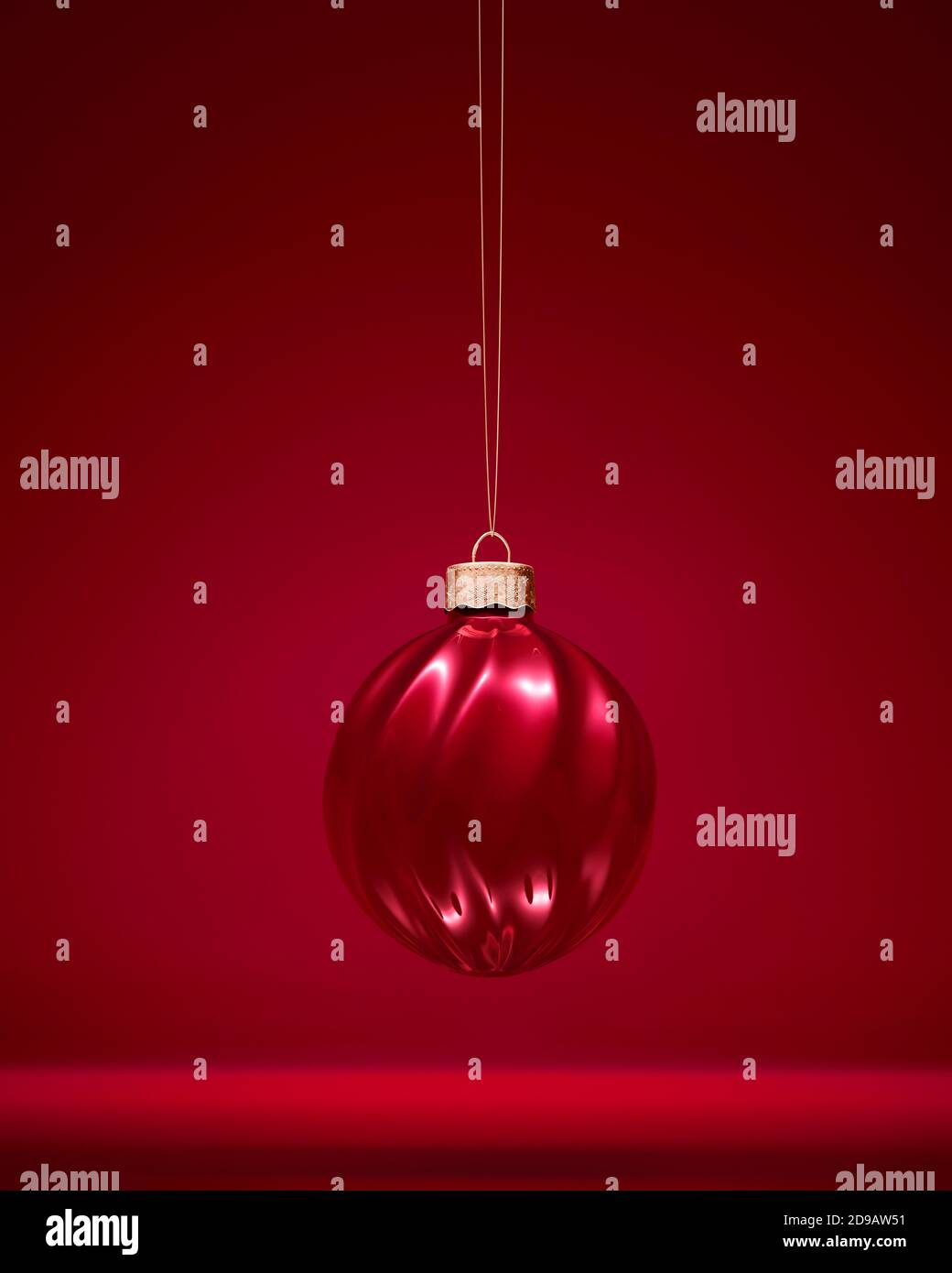 Burgundy red twisted ribbed Christmas ball. Glossy ornament. Red shaded background. Christmas decoration, festive atmosphere concept. Stock Photo
