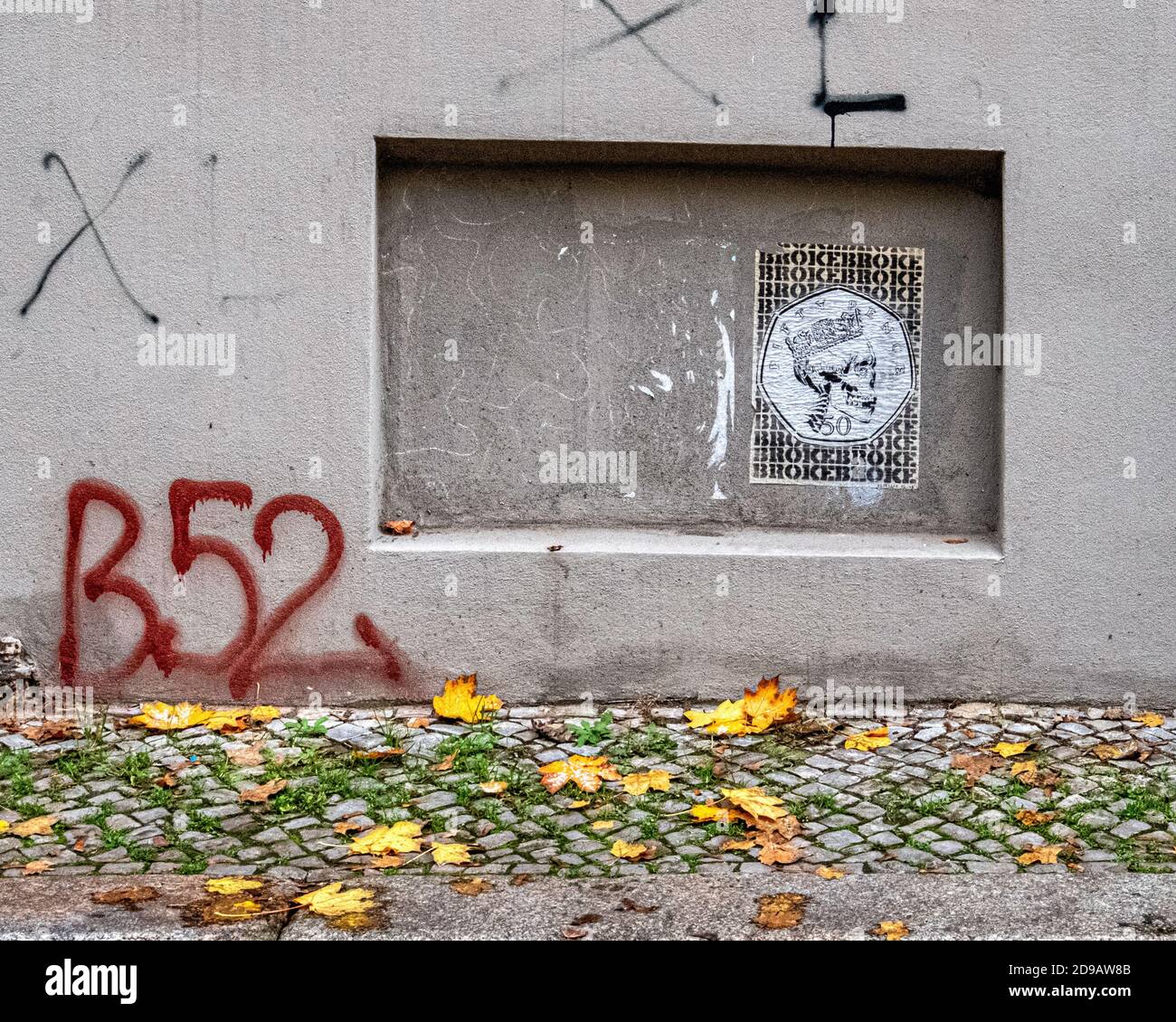 Urban detail, Skull street art paste-up, graffiti covered wall and cobbled pavement in Autumn in Mitte,Berlin,Germany Stock Photo