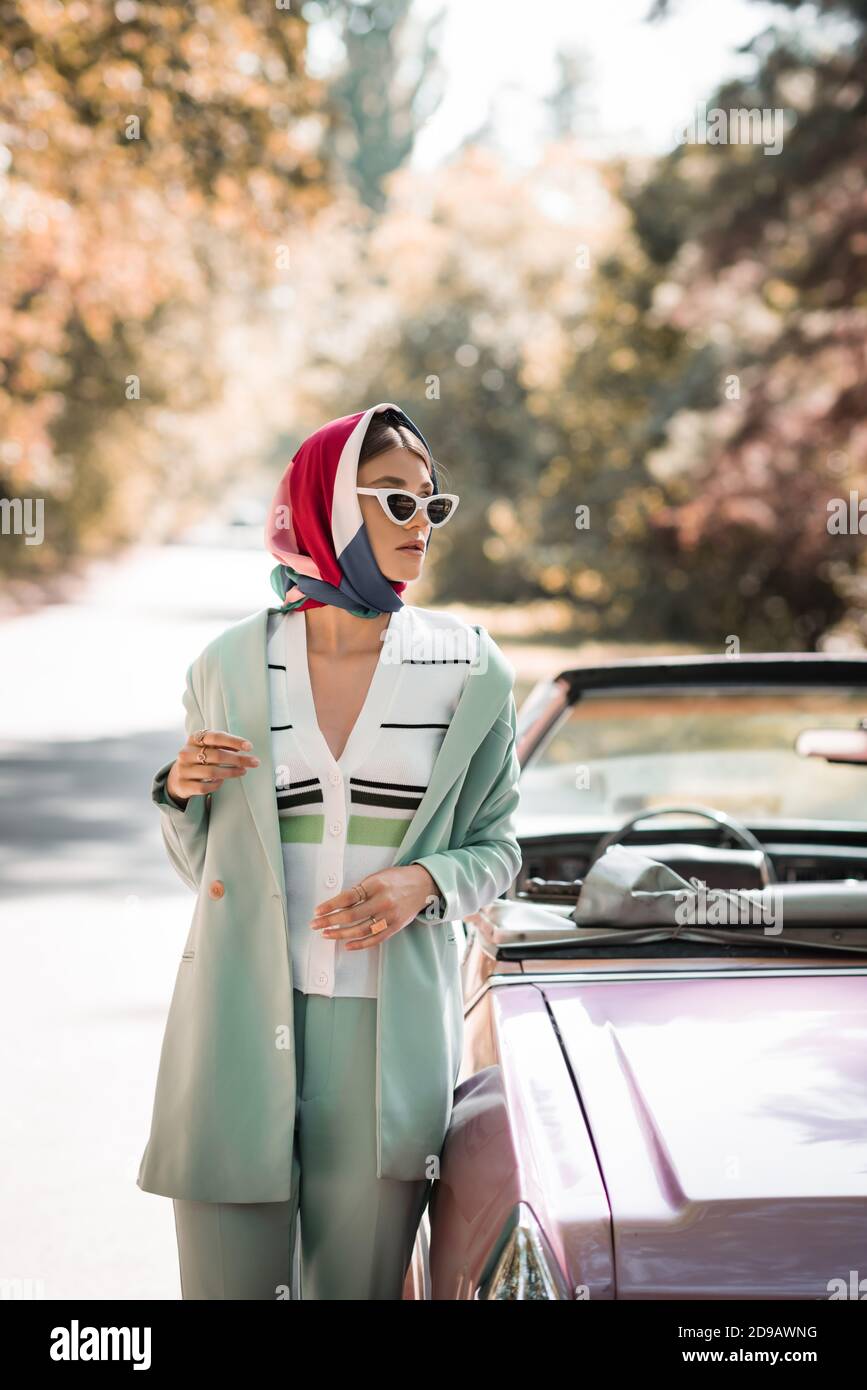 Fashionable woman in headscarf and sunglasses standing near car on road  Stock Photo - Alamy