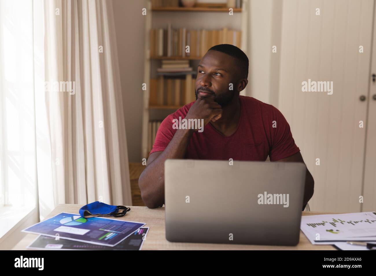 Thoughtful  african american man looking out of window with laptop Stock Photo