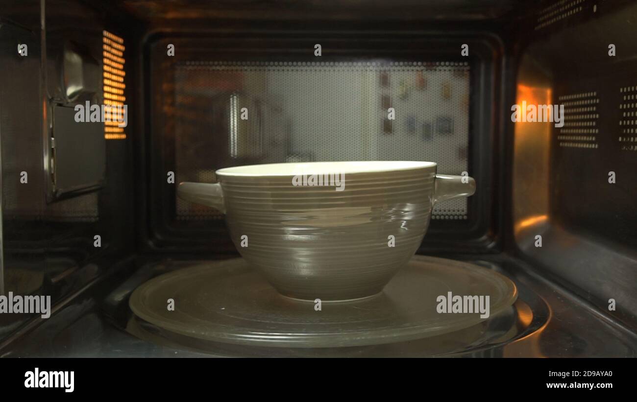 Ceramic bowl with some food heats up in the microwave spinning on turntable tray inside oven