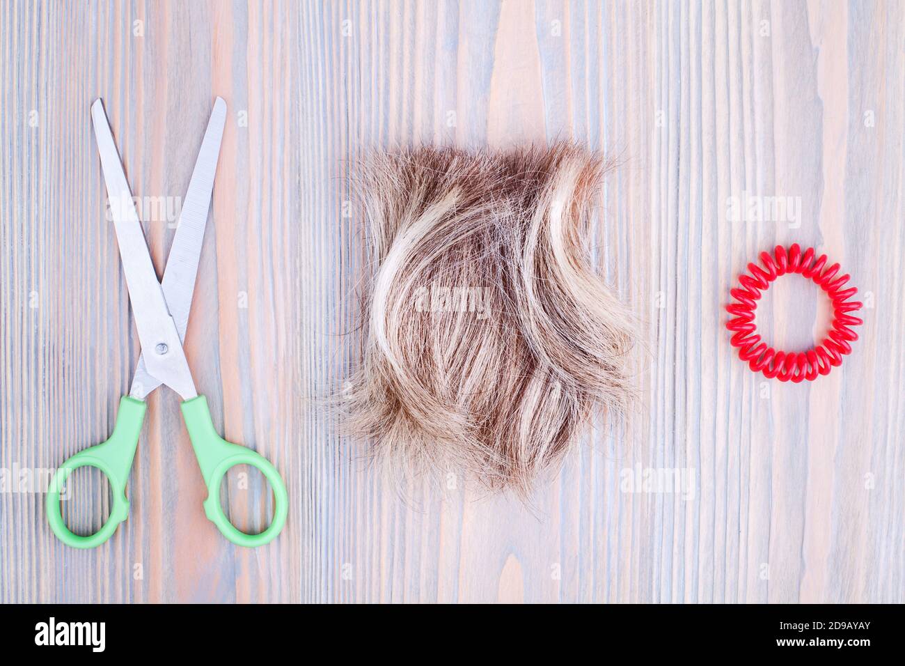 Blond hair lock, scissors, scrunchie light wooden background close up, cut off blonde hair curl on bright wood, shears, spiral hair band barrette Stock Photo