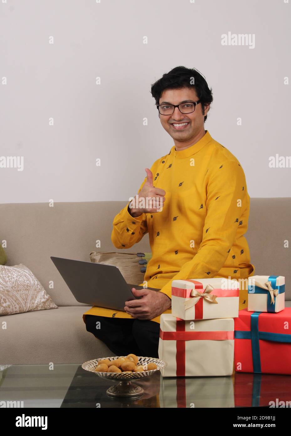 Young man in spectacles and tradional wear sitting at home using laptop. Stock Photo