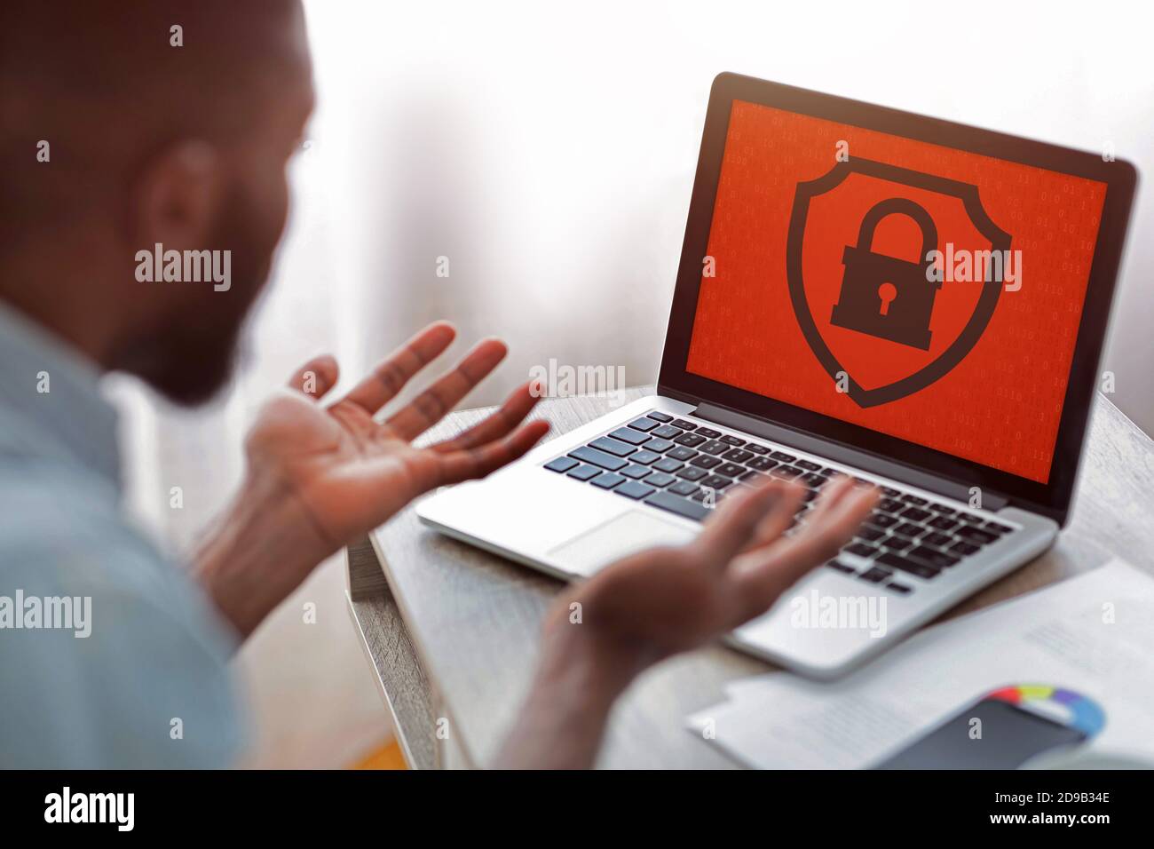 Worried african american man looking at computer with red screen and closed lock at workplace Stock Photo