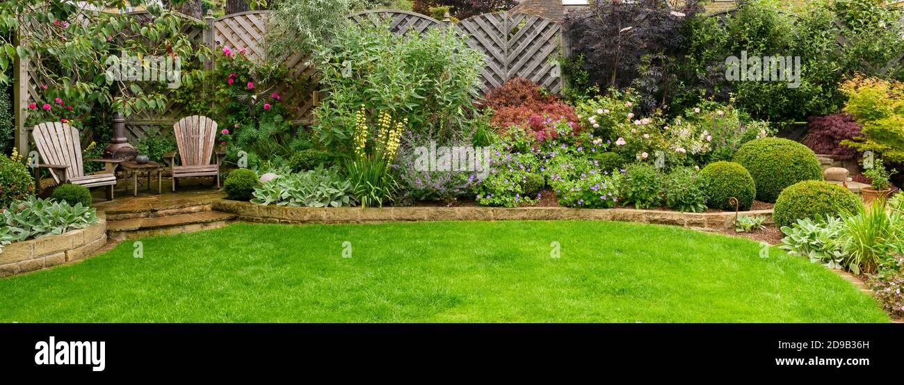 Landscaped private garden (contemporary design, summer flowers, border plants & shrubs, patio furniture, curving lawn, fence) - Yorkshire, England, UK Stock Photo