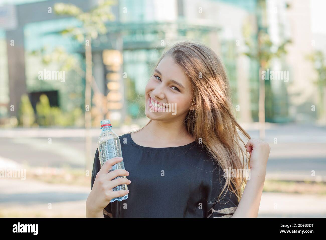 Thirsty. Cute teenager holding a bottle of water in the city smiling. Teen  girl, woman laughing happy about to drink water, posing touching hair city  Stock Photo - Alamy
