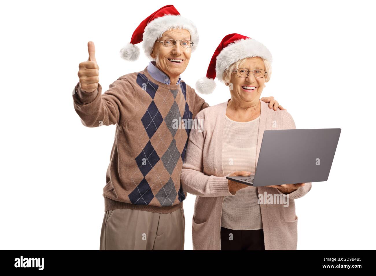 Elderly man showing thumb up and an elderly woman holding a laptop, both wearing christmas hats isolated on white background Stock Photo
