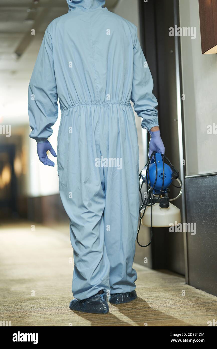 Back view of male specialist in blue suit with disinfectant going to sanitize room in hotel. Coronavirus and quarantine concept Stock Photo