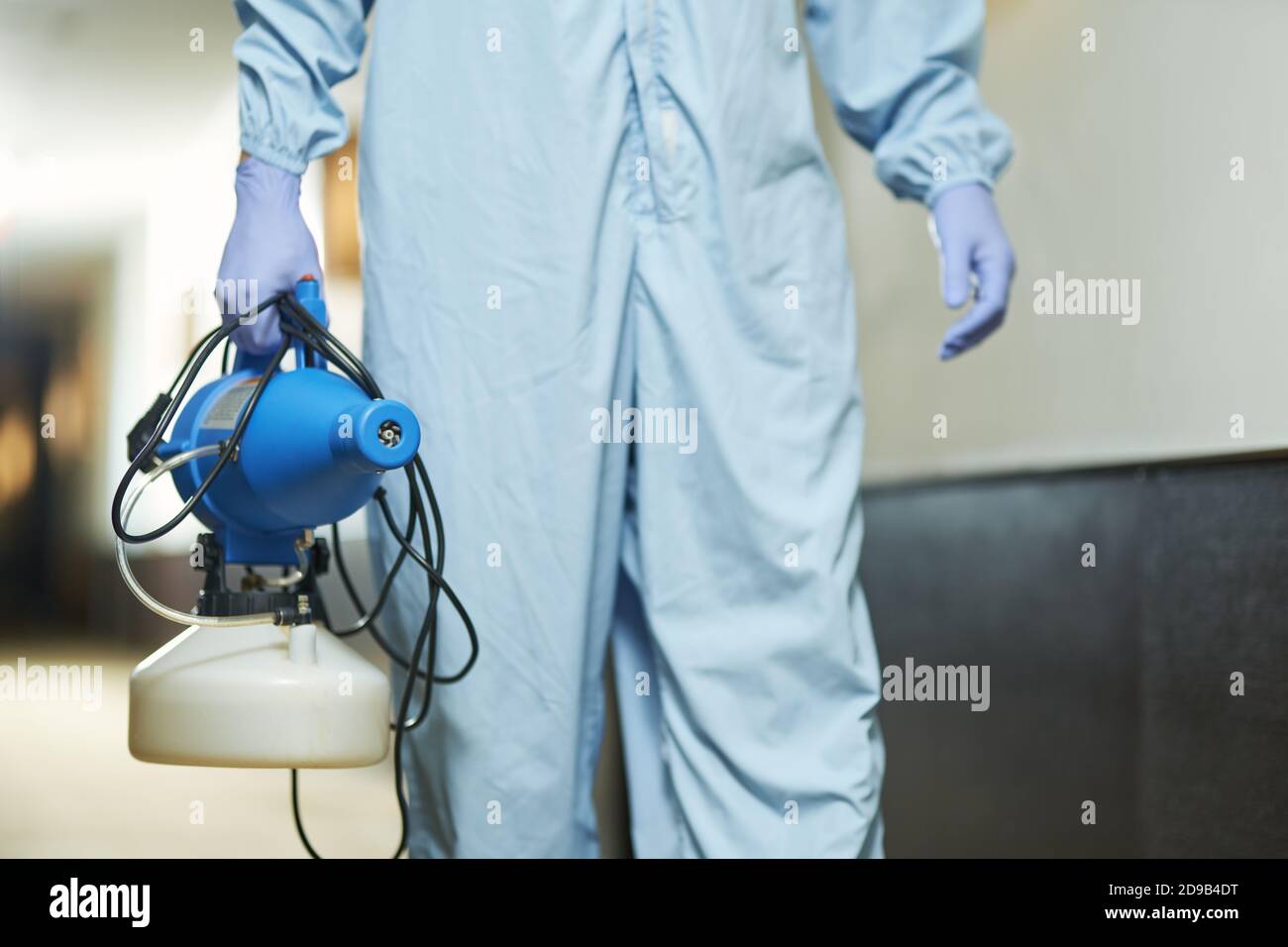 Close up of worker holding disinfectant while walking in hotel corridor. Coronavirus and quarantine concept Stock Photo