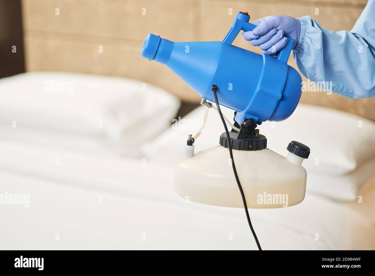 Close up of male hand in protective glove standing with disinfectant near bed in hotel room. Coronavirus and quarantine concept Stock Photo