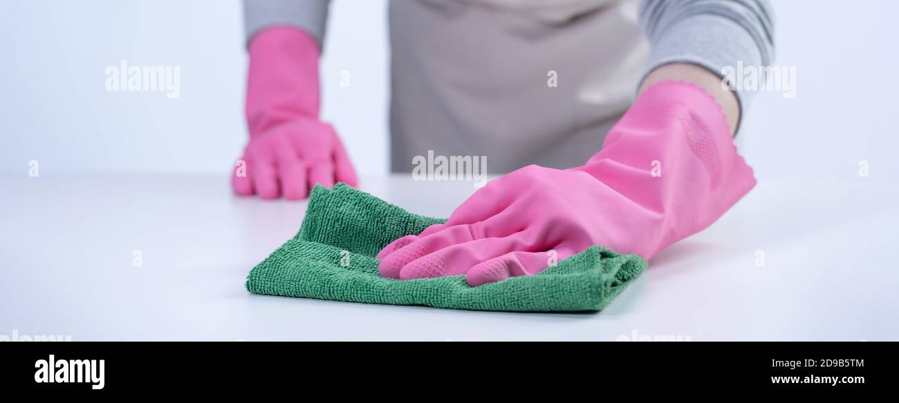 Young woman housekeeper in apron is cleaning, wiping down table surface ...