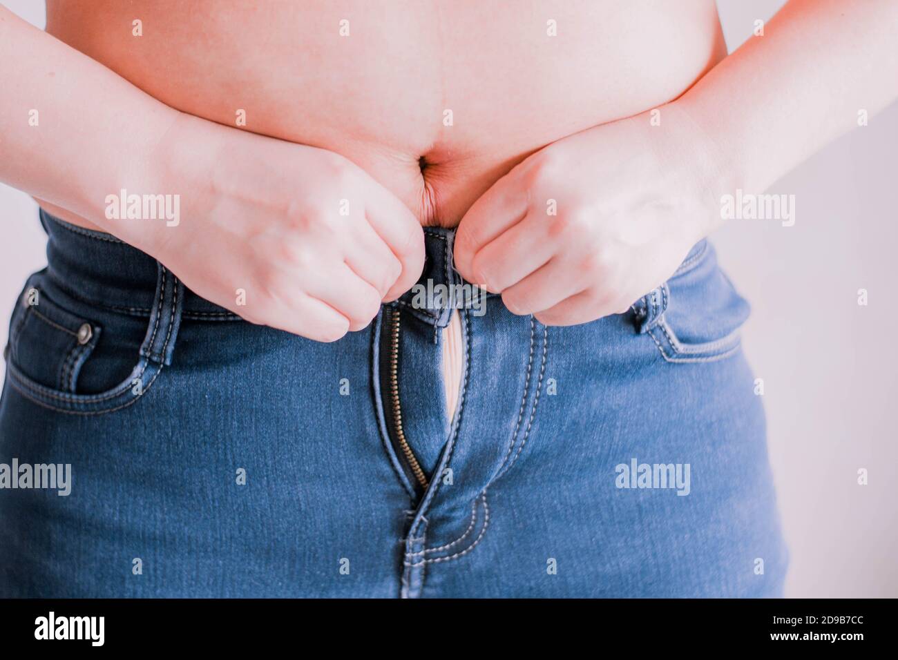 Woman after childbirth is trying to put on jeans. Her stomach is too