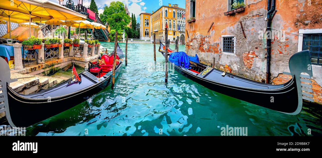 Scenic panoramic landscape with gondolas by wharf of open cafe terrace on Grand Canal in Venice. Italy Stock Photo