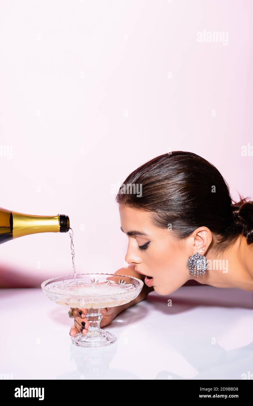 woman drinking champagne from glass near bottle on white Stock