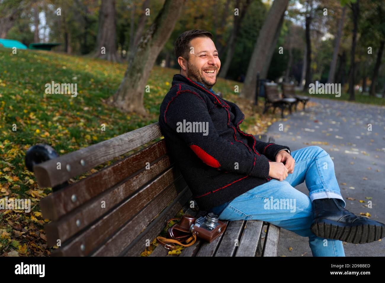 Smiling man sitting on the bench in the park at autumn with vintage