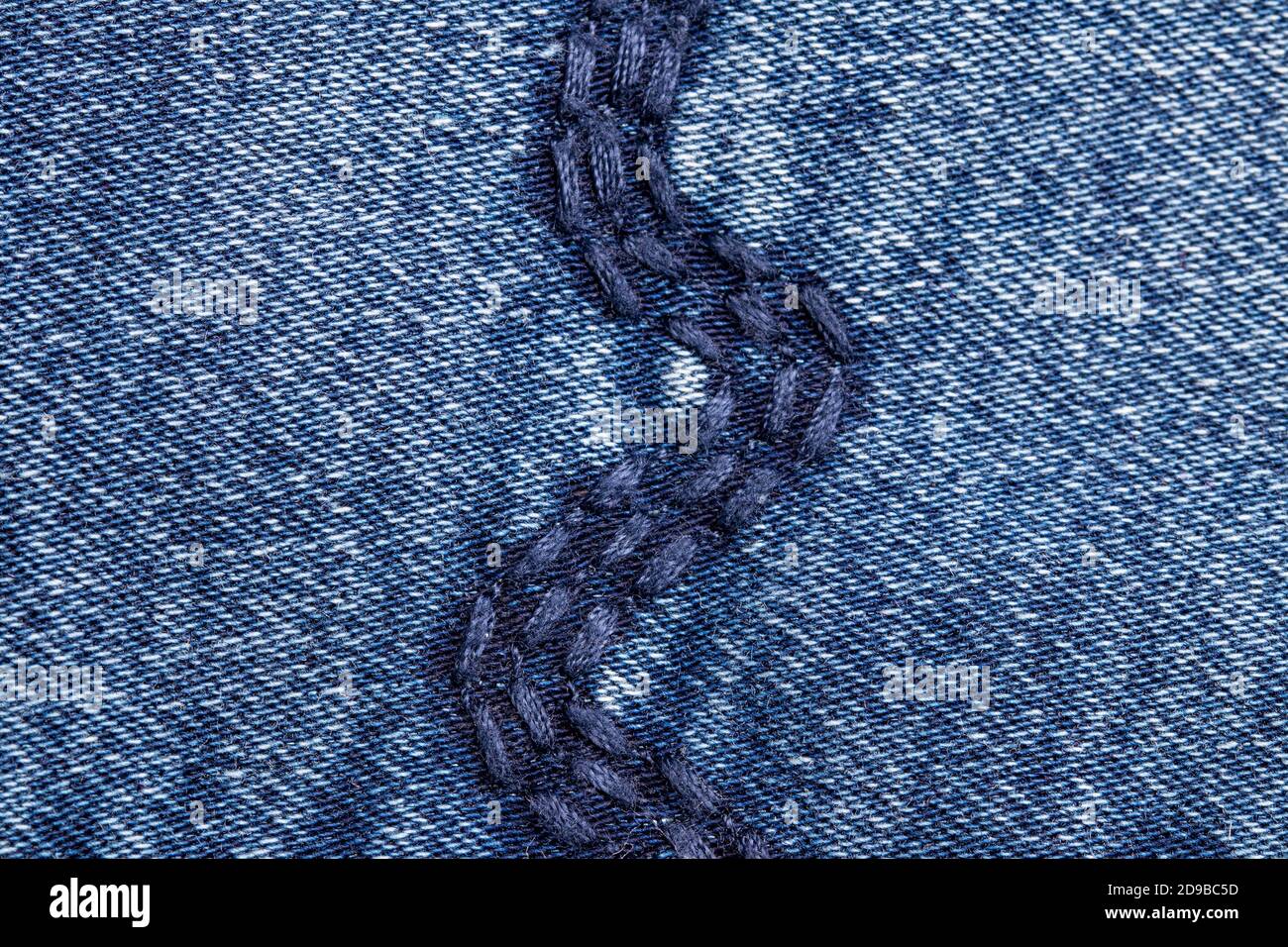 Denim background texture. Close-up of details of a light blue jeans fabric jean surface with fashion embroidery in blue colours. Macro. Top view. Beau Stock Photo