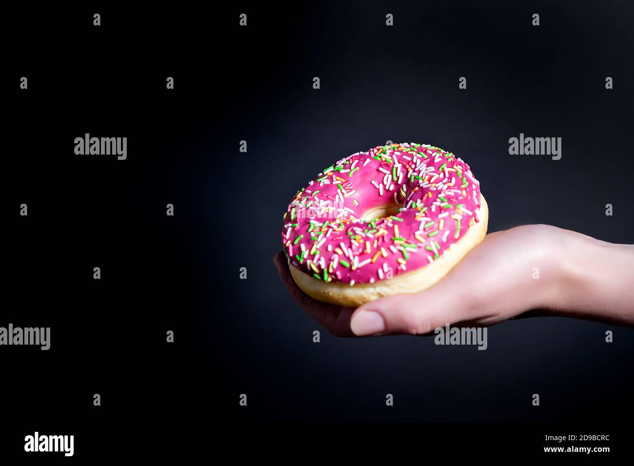 Donut on a dark background. Donut with pink frosting. The cook's hand holds  a pink doughnut. Selective focus. Close up Stock Photo - Alamy