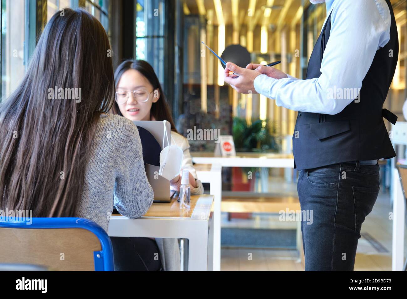 Caucasian waiter taking clients order in a restaurant during coronavirus outbreak. New normal in restaurants. Coronavirus pandemic. Stock Photo