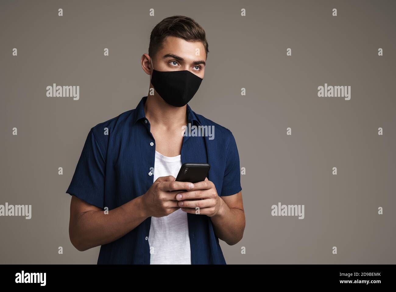 Image of caucasian guy in face mask using mobile phone isolated over grey background Stock Photo