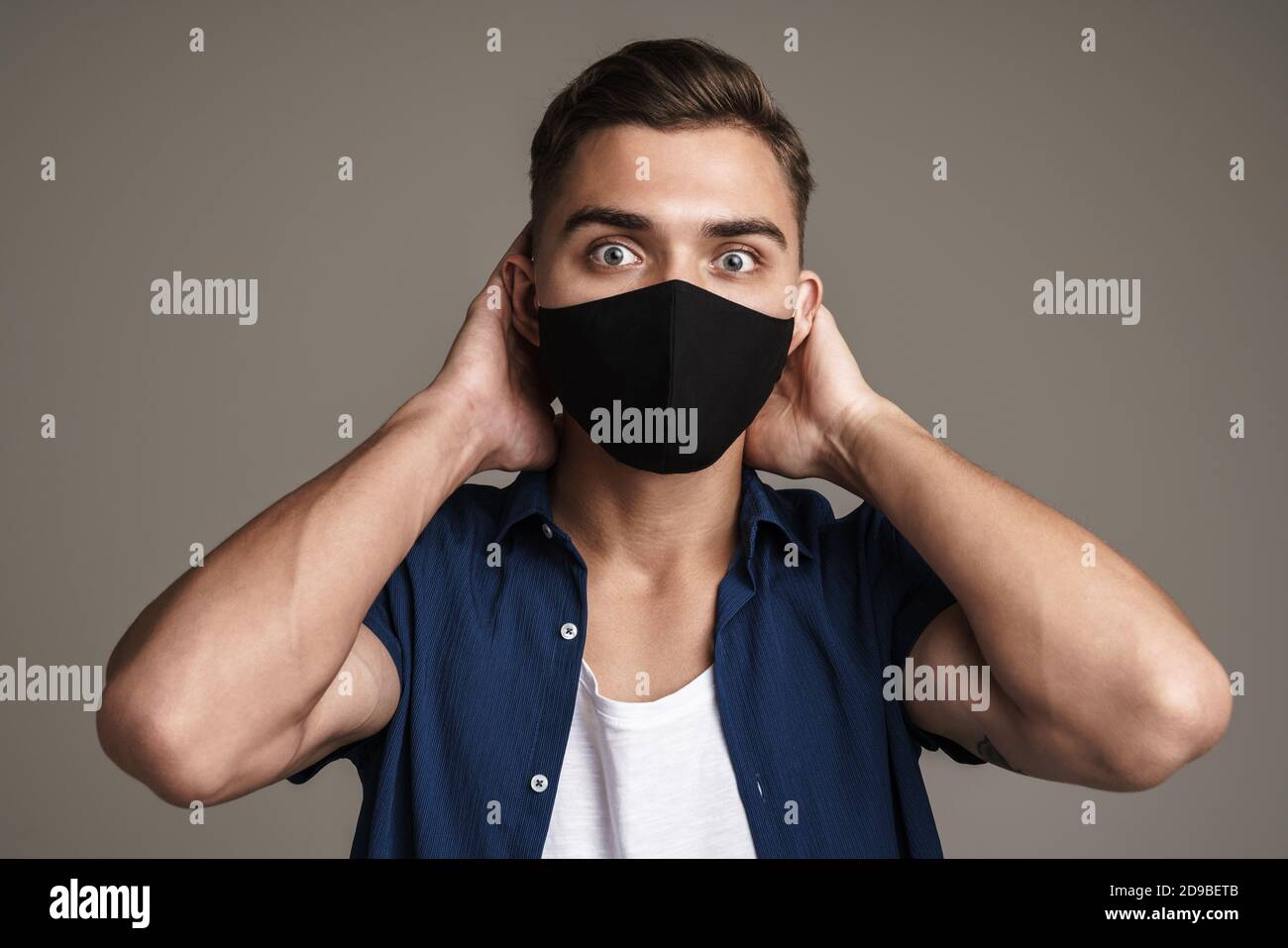 Photo of scared young man isolated over grey wall background in a mask Stock Photo