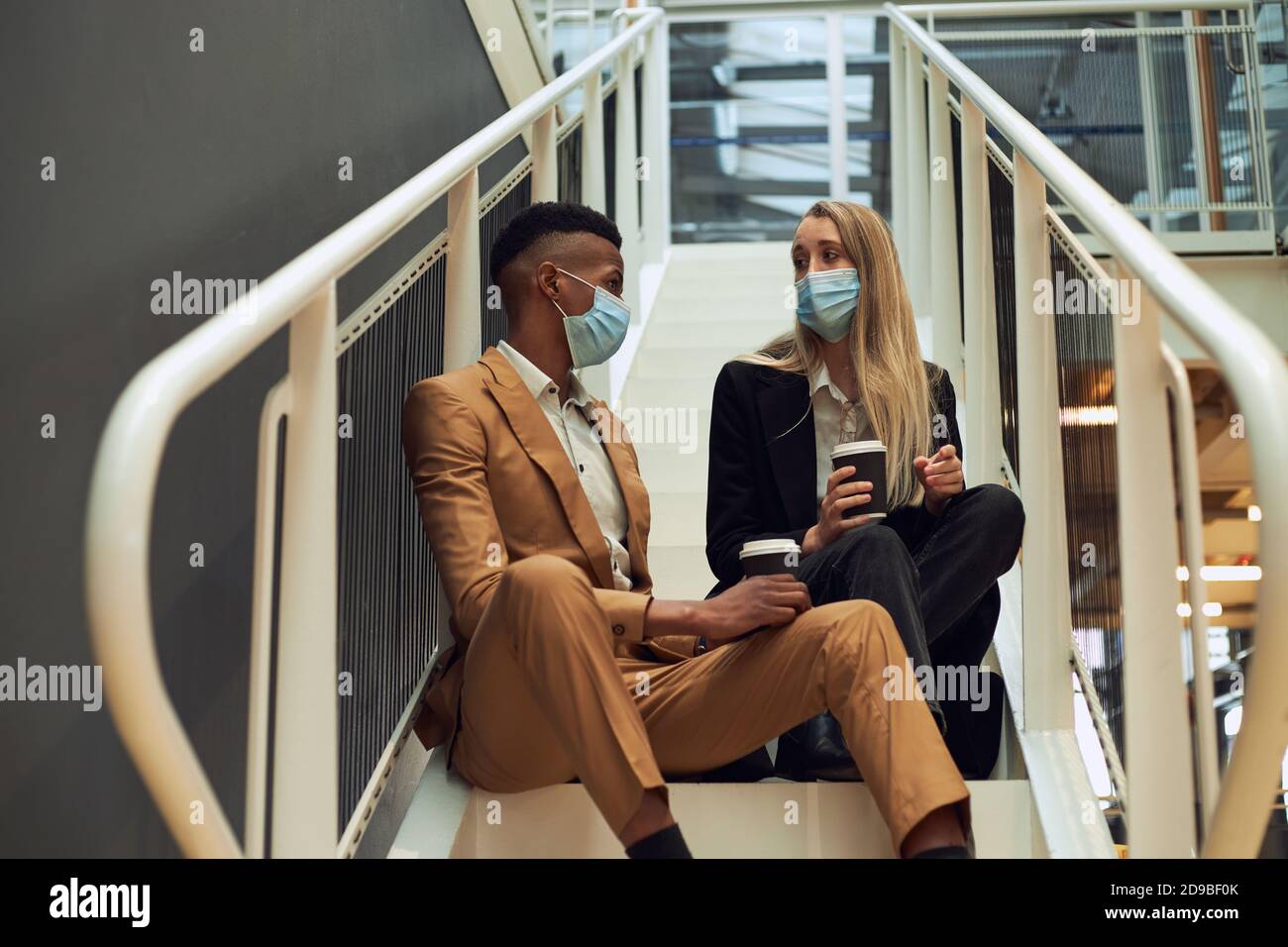 Business Couple Wearing Masks Meet On Office Stairs During Break In Office During Pandemic Stock Photo