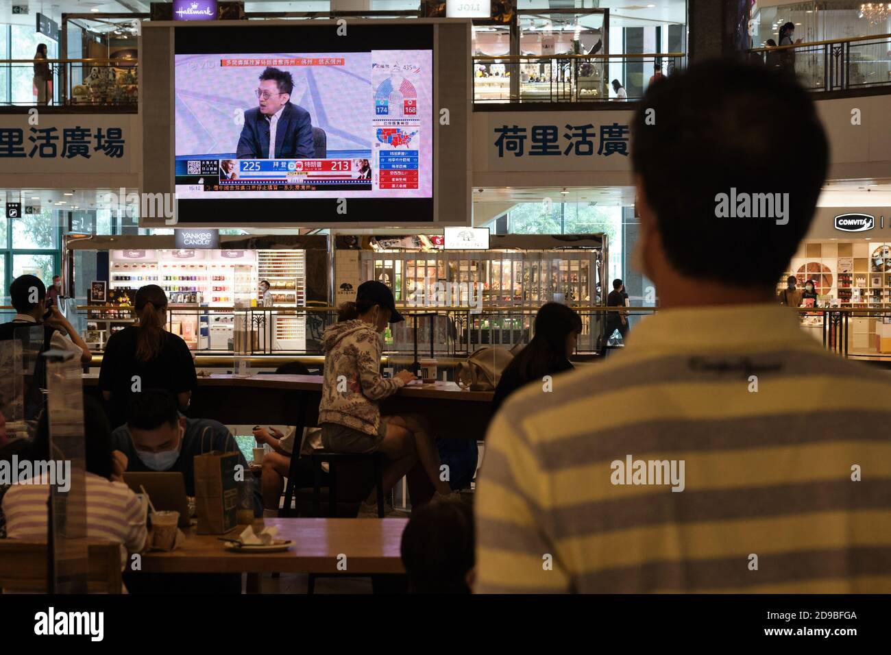 A man watches the live news of the US Presidential elections showing on a TV screen at a shopping mall in Hong Kong. Stock Photo