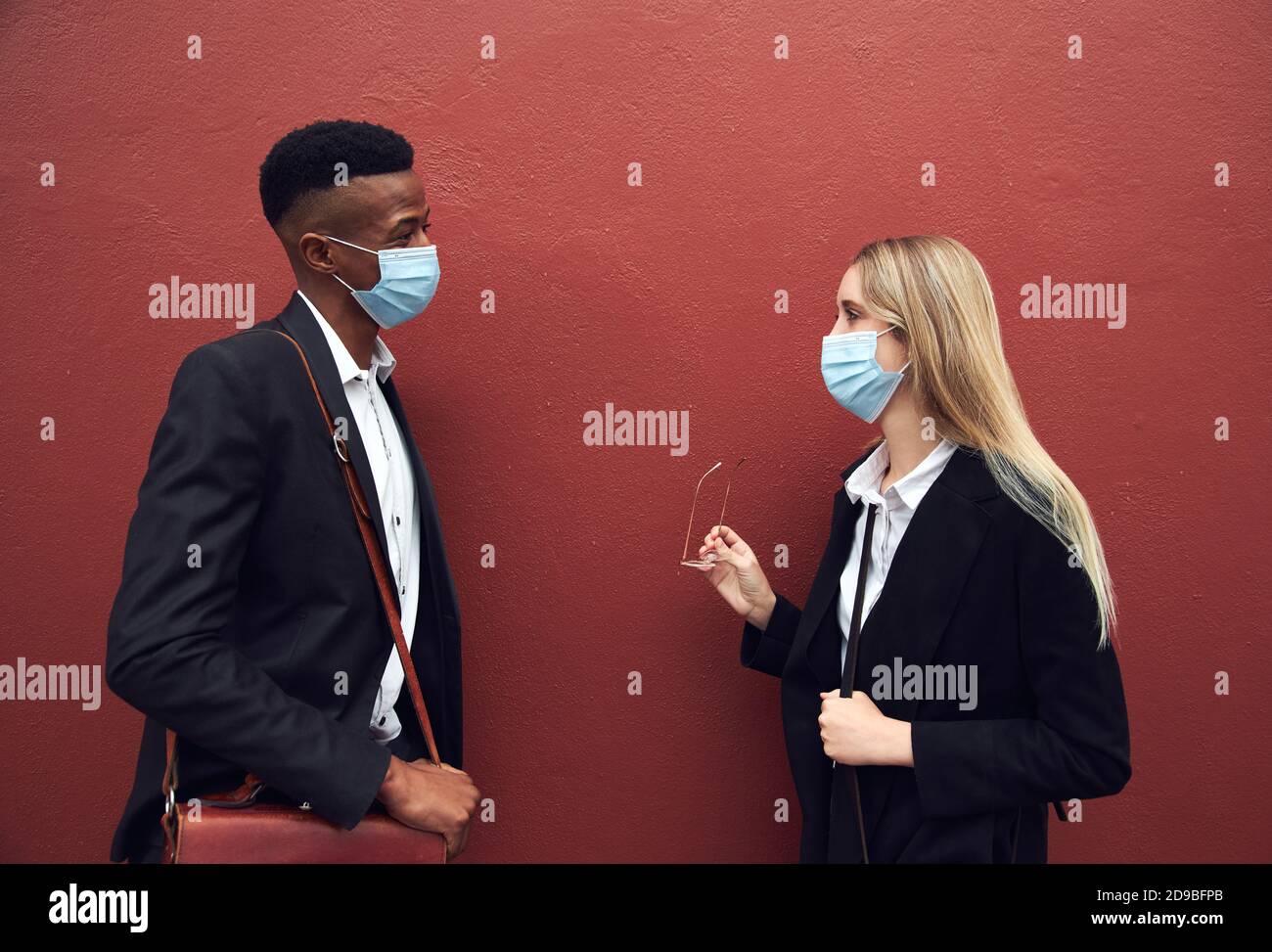 Businessman And Businesswoman Wearing Masks Standing By Wall Outside Office During Health Pandemic Stock Photo