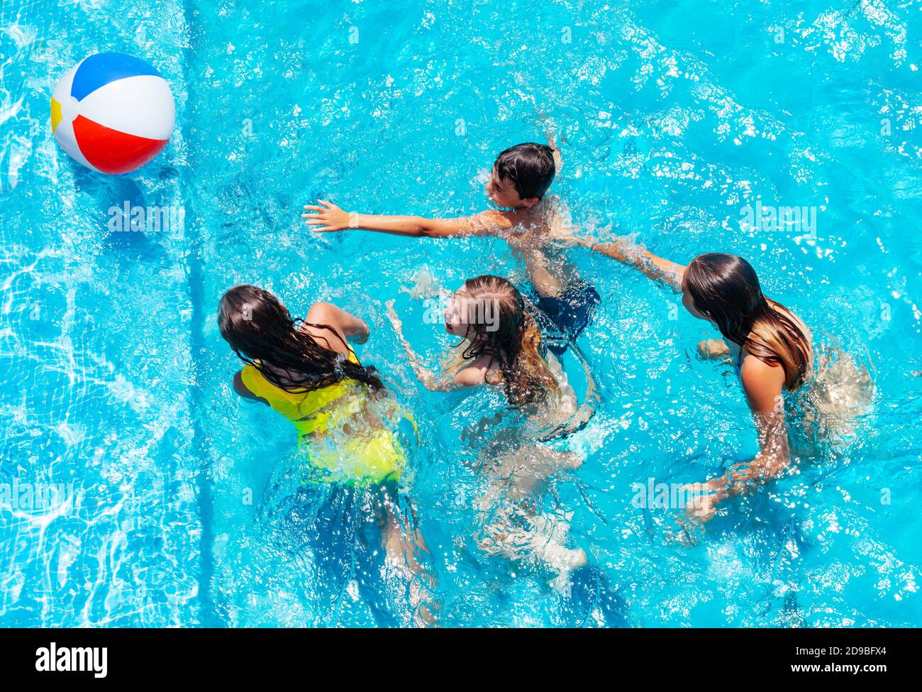 Group of many kids jump after inflatable ball, play in swimming pool