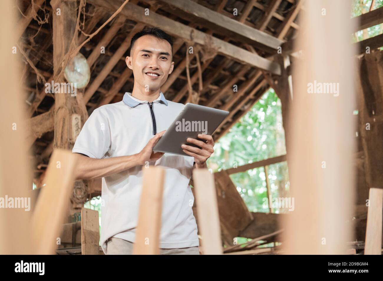 Selective focus of Asian men looking at the camera while using a tablet pc in a furniture workshop Stock Photo