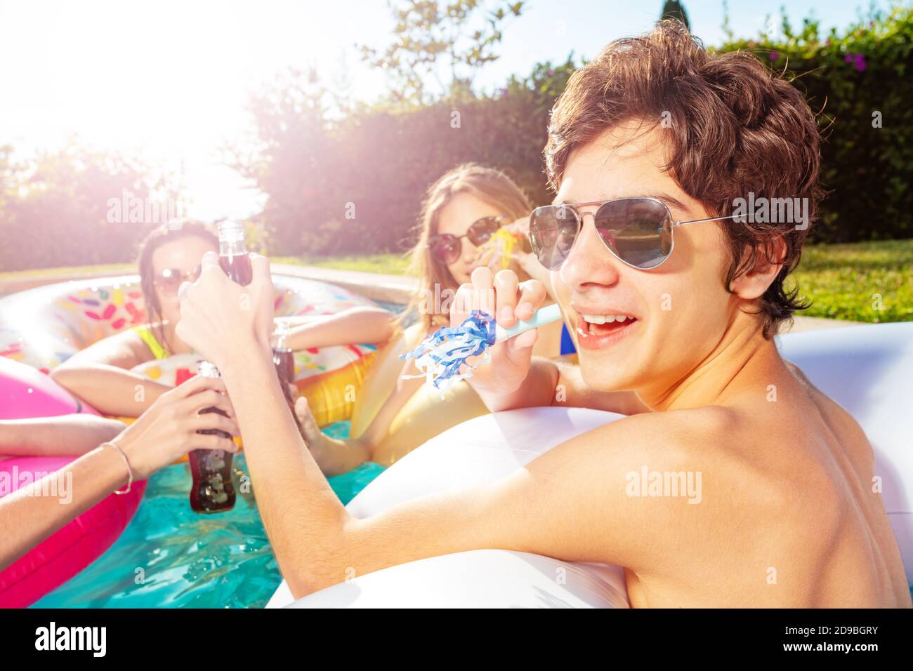 Teenage boy blow noisemaker party in the swimming pool with friends
