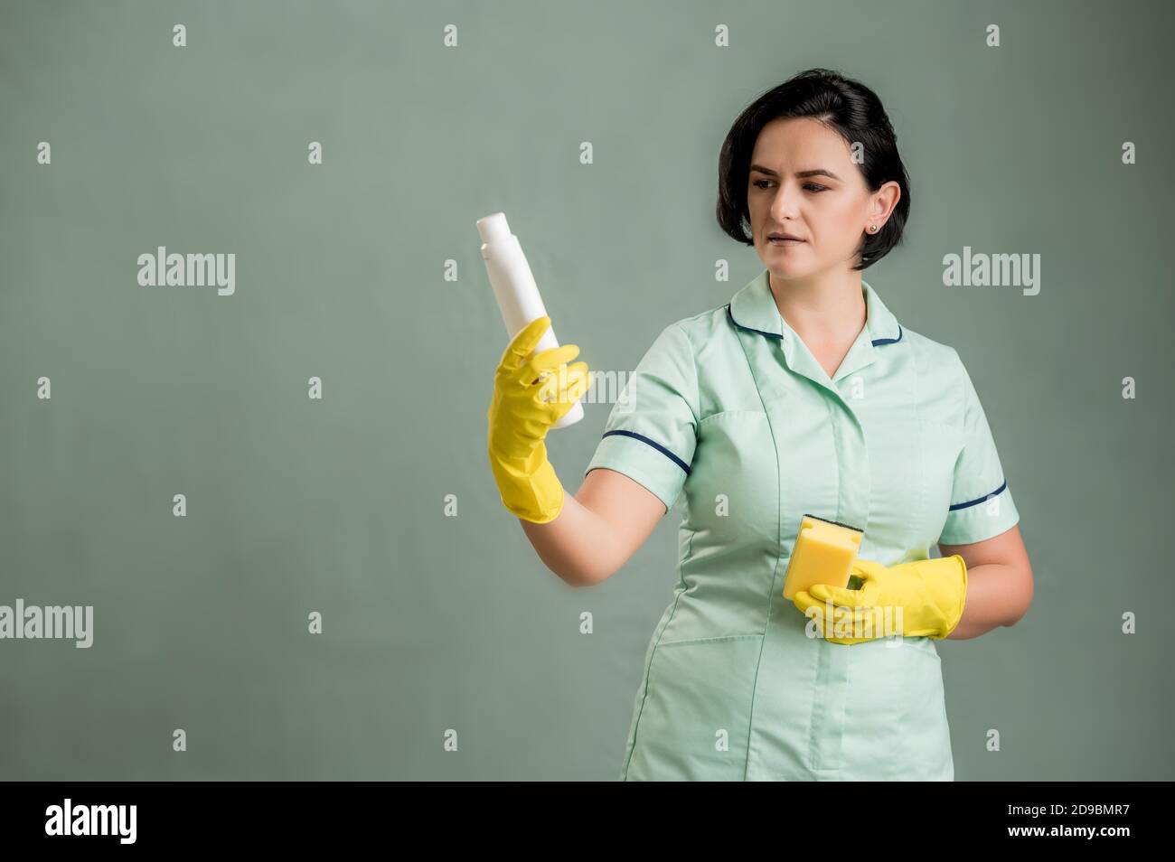 Young cleaning woman wearing a green shirt and yellow gloves, holding ...