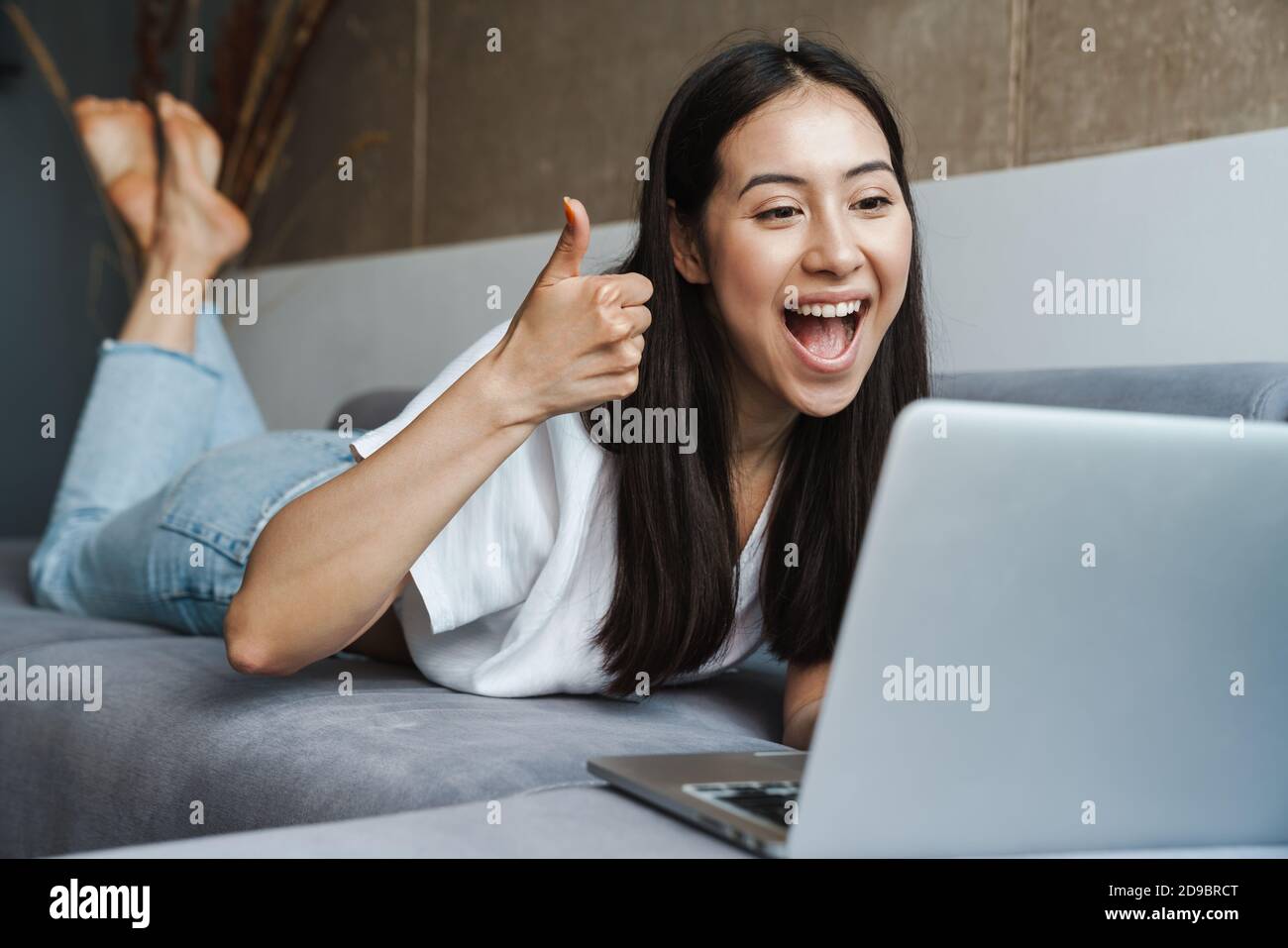 Happy young woman on a video call through laptop computer while laying ...