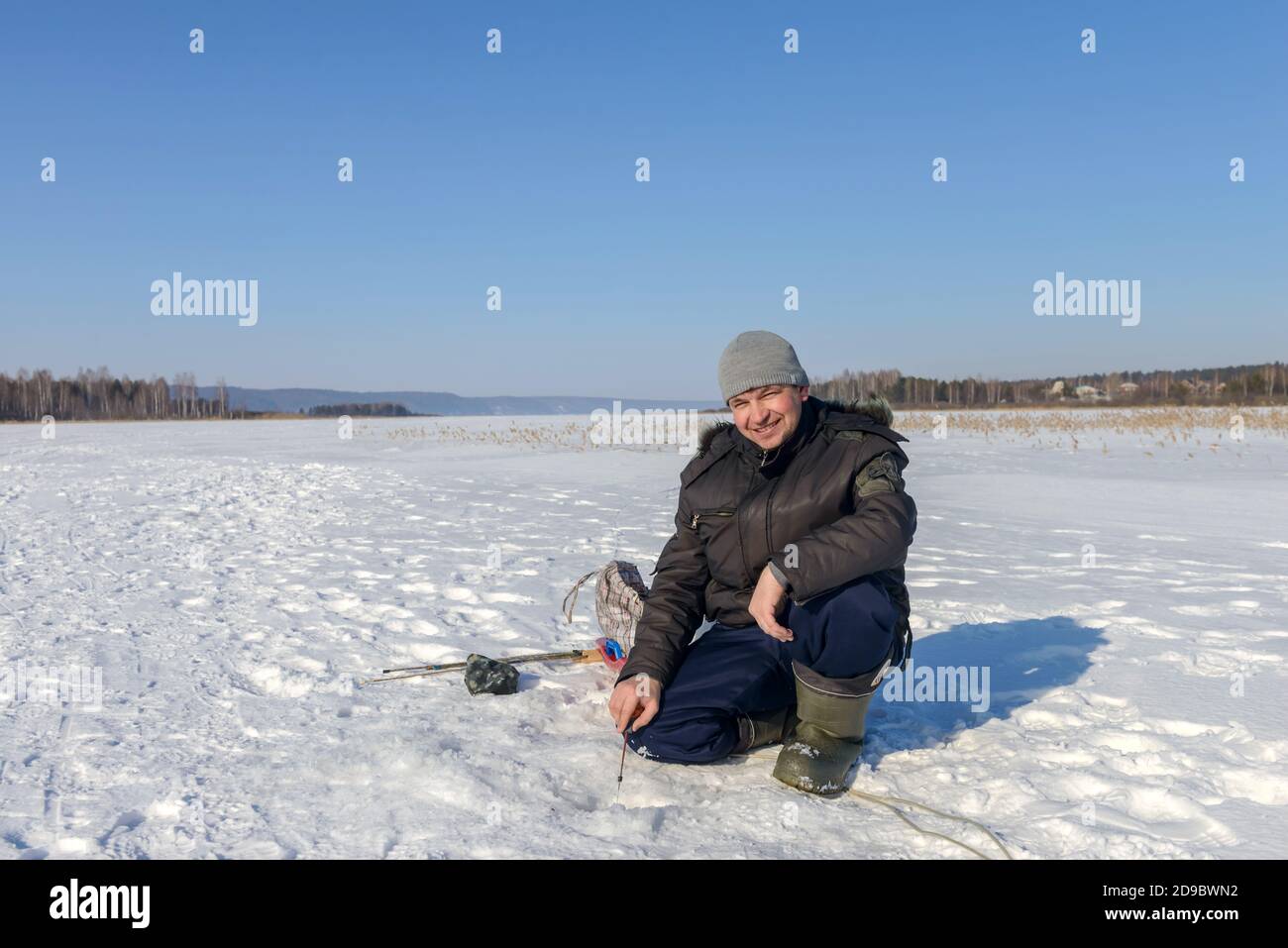 Fisherman near the ice hole catches fish on the ice. Winter fishing. Ice fishing. Russia. February 20, 2016 Stock Photo